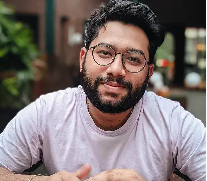 Hombre barbudo con gafas sonríe a la cámara, camiseta lila.