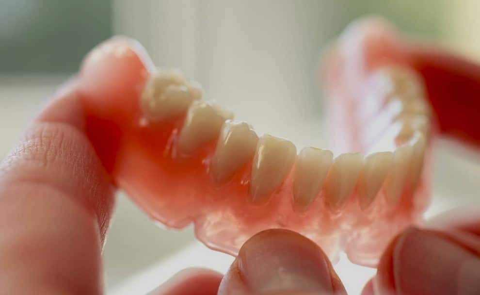 Primer plano de una dentadura postiza rosada sostenida entre los dedos, mostrando los dientes artificiales en detalle.